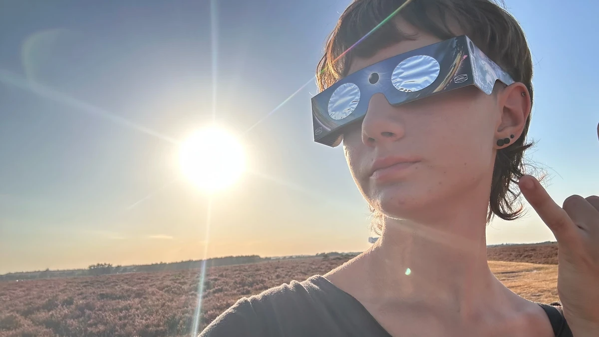 A teenager wearing certified eclipse glasses on New Forest heathland with the bright sun low in the sky behind