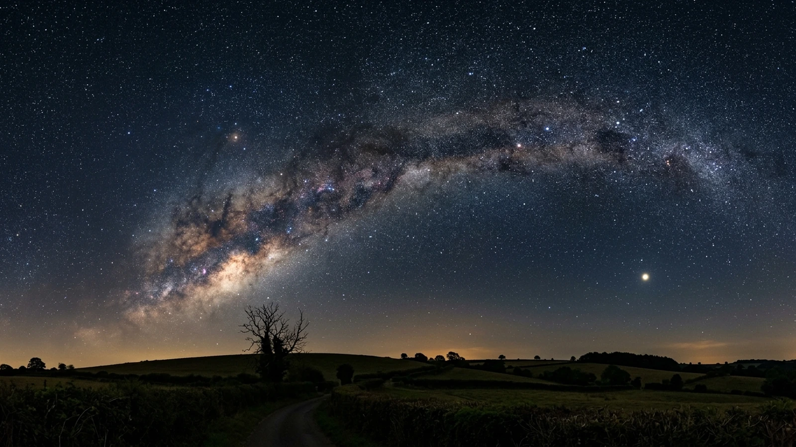 The late-summer Milky Way arching over a dark British countryside horizon with Saturn bright in the south