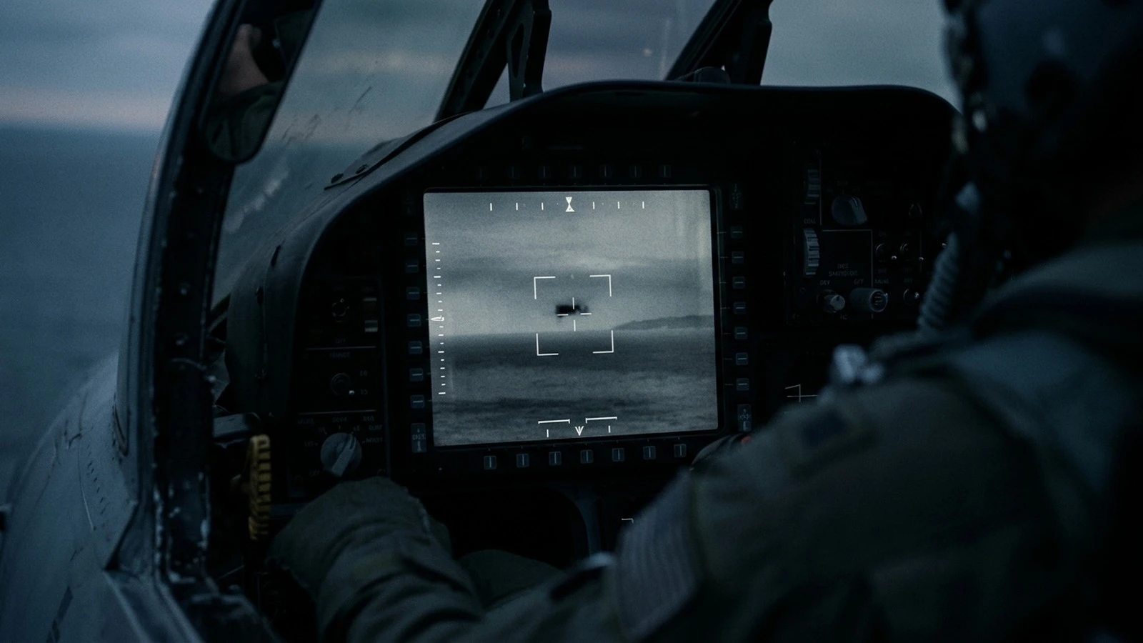 A monochrome infrared targeting display with a small dark object held in a tracking reticle above a hazy sea horizon, with heads-up display markings around the edge