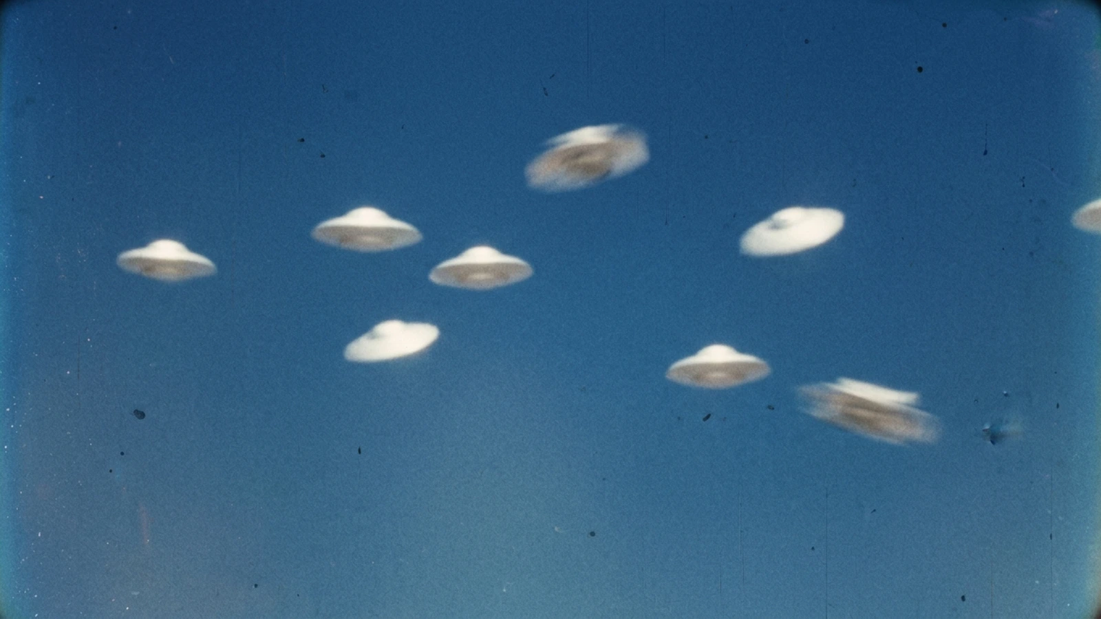 Bright white objects circling in formation against a deep blue sky, in the style of 1950s colour film